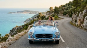 Couple souriant en décapotable vintage sur une route côtière méditerranéenne lors d'un voyage de Marseille à Menton.